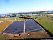 Aerial view of a solar farm with part of a wind farm in the background