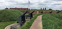 Cannons next to grassy embankment in front of brick fort above which the US flag is flying