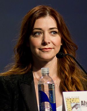 Hannigan seated behind a microphone and a bottle of water