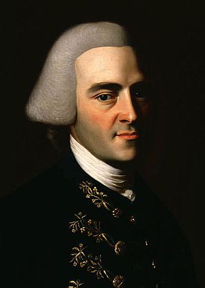 Half-length portrait of a man with a hint of a smile. His features suggests that he is in his 30s, although he wears an off-white wig in the style of an English gentleman that makes him appear older. His dark suit has fancy embroidery.