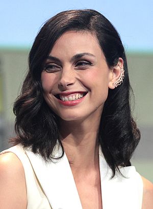 A smiling woman with shoulder-length, dark brown hair and wearing a white blouse looks off to her right