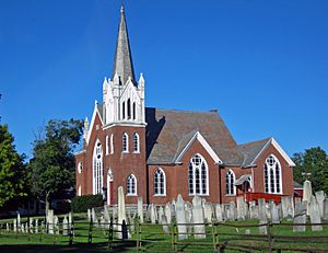 A brick church with white tower and a cemetery in front