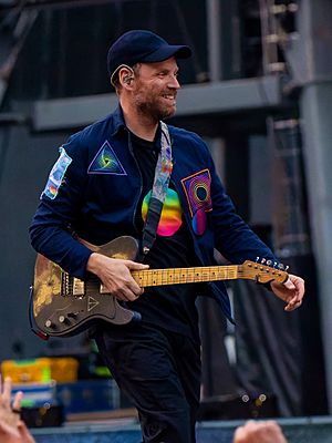 A man wearing a dark blue cap and jacket walks with his guitar