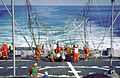 A large net on the back end of a ship. Several orange clad crewmen are working to free a white singed object from the net.