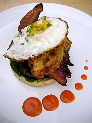 A bacon and oyster pile with egg on top on a plate surrounded by small dots of sauce
