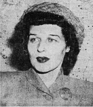 Portrait of a woman with short hair wearing a pillbox hat and 1940s style suit with a large round broach at the edge of the left lapel.