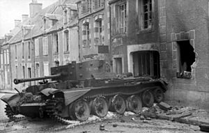 A tank, with debris strewn around it, is in front of a damaged and fire scorched house. The tank is partly on the pavement and partly on the road.