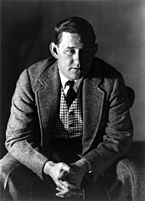 Black and white photograph of writer John O'Hara. He is sitting on a chair and leaning forward, his face partly in shadow. He is wearing a dark suit with a plaid vest, white shirt, and black tie. His hands are clasped in front of him.