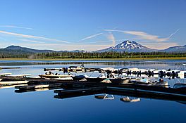 Boat dock with boats with calm water on a sunny day.  Mount Bachelor is in the distnace.