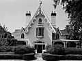 A black and white photograph of a house with steeply roofed gables. Gingerbread molding frames the gables, whose ends contain windows with rounded tops.