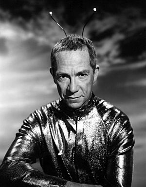 A black-and-white photo of Walston as a Martian, with a shiny suit and antenna on his head