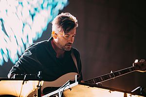 Bonobo appearing to perform onstage, holding an acoustic guitar
