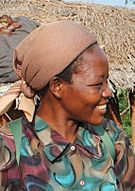 Angélique Namaika smiling in a village, wearing a green shirt and brown headdress.