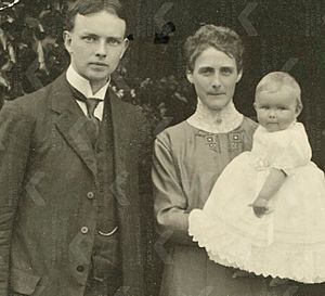photograph of a man standing next to a woman, who is holding a baby
