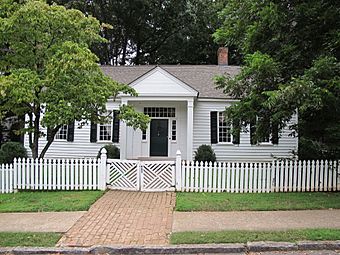 Photo of a one-story home painted white with black shutters with a white picket fence in front.