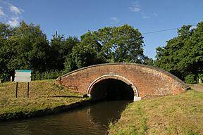A brick arch bridge crossing a canal. In the foreground, this canal joins with another