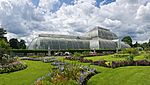 A large greenhouse with rounded ends and sides sits in the middle of groomed grass and flower beds.