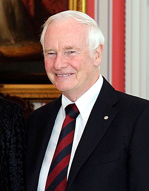 Photograph of Johnston smiling. He is wearing a dark suit with a red and black striped tie.