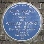 A Blue plaque on a brick wall with the words "John Beard C1717 - 1791 Singer and William Ewart 1798 - 1861 Promoter of Public Libraries