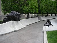 Short white walls with an adult lion sculpture sitting on the left and a lion cub on the right