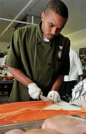US Navy 100428-N-5812W-003 Culinary Specialist 3rd Class Corey Hartfield prepares a filet of farm-raised pacific steelhead salmon