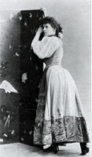 Young white woman in 1890s day clothes, leaning pensively against a column