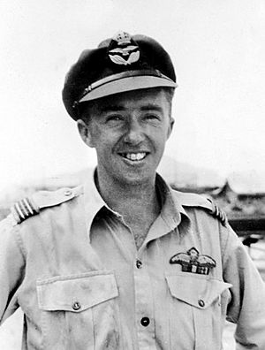 Outdoor half portrait of grinning man in light-coloured uniform with pilot's wings on left pocket, wearing peaked cap