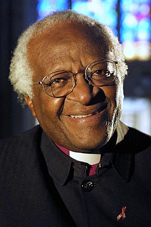 Portrait photograph of Desmond Tutu wearing glasses and a black coat with a clerical collar