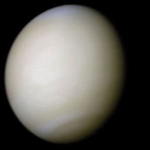 Venus in approximately true colour, a nearly uniform pale cream, although the image has been processed to bring out details. The planet's disc is about three-quarters illuminated; almost no variation or detail can be seen in the clouds
