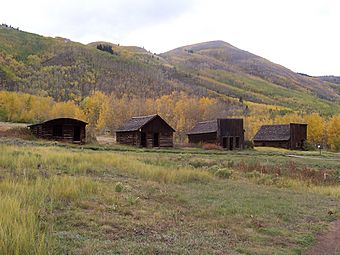 Four small old wooden buildings seen at some distance with high hills in the background.