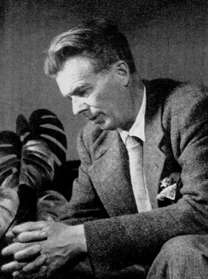 Monochrome portrait of Aldous Huxley sitting on a table, facing slightly downwards.
