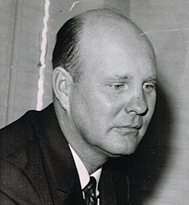 Candid black and white head and shoulders photograph of Ivy wearing a dark suit and looking down slightly