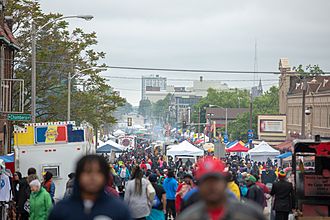 A large street festival in Milwuakee, Wisconsin. Much of the crowd is African American, and cooking smoke can be seen rising from food trucks and stands parallel to the street.