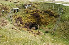 A deep pit surrounded by an unsubstantial-looking wire fence