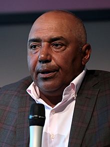 Color photograph of man (Marvin Lewis) wearing a suit and speaking into a microphone.